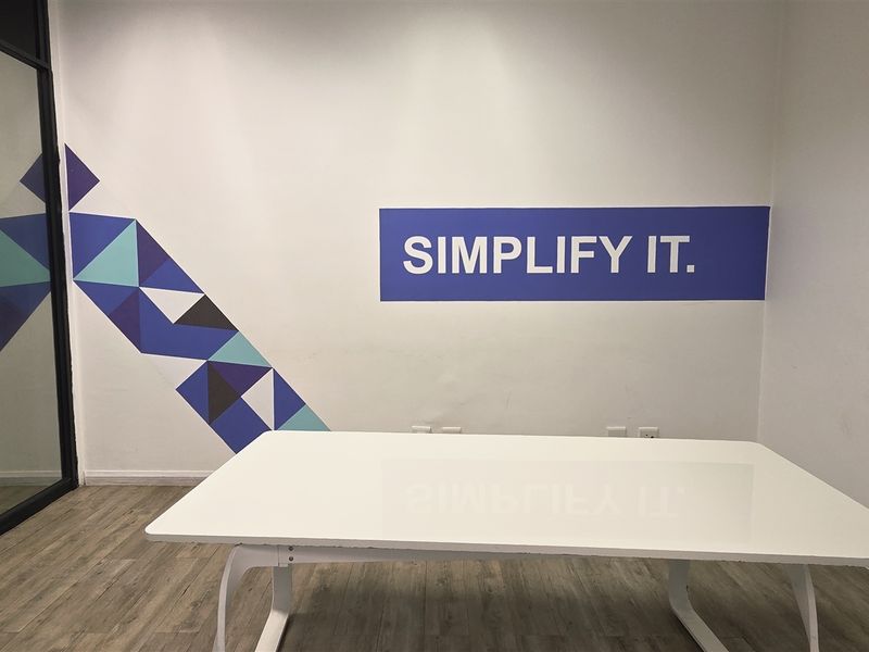A modern office space featuring laminate flooring, a glass partition wall, and clean white walls with decorative branding.