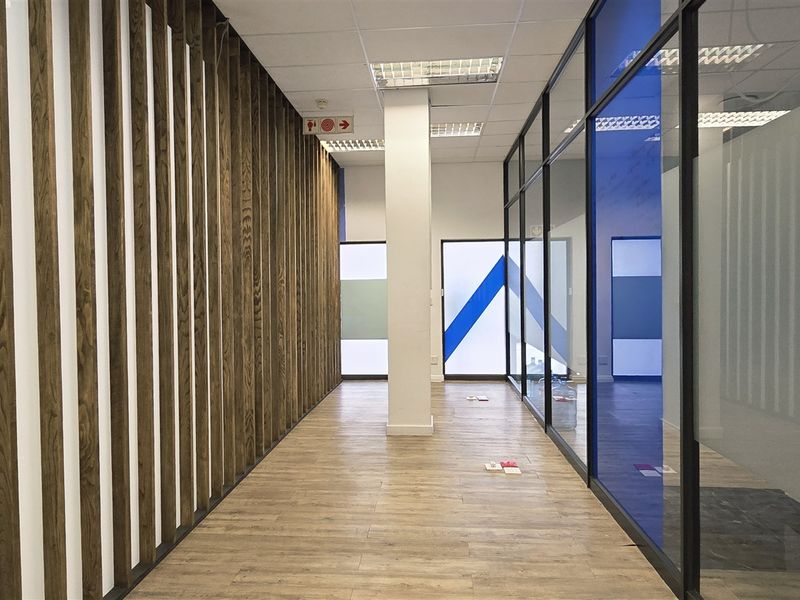 A modern office hallway featuring wood slat wall paneling, glass partitions, and durable laminate flooring with a clean, professional aesthetic.