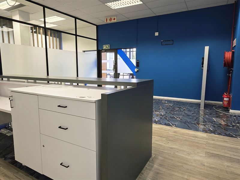 Modern office reception area featuring a built-in desk, glass partitions, and a combination of tiled and laminate flooring in a professional workspace.
