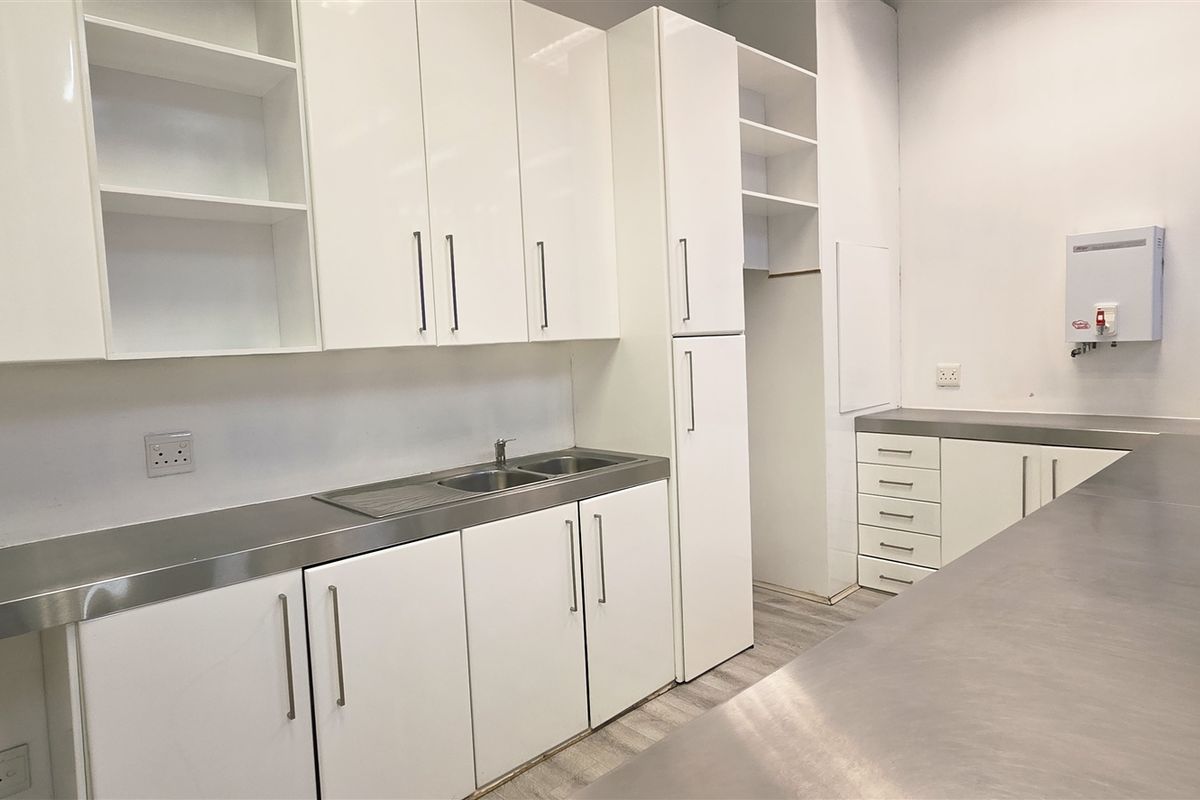 A clean, modern office kitchenette featuring white cabinetry, stainless steel countertops, an integrated sink, and a wall-mounted water heater.