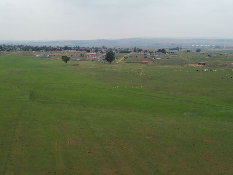 An aerial view of a large, open commercial vacant land plot featuring expansive grassland and surrounding rural landscape.