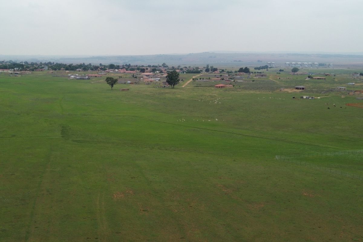 An aerial view of a large, open commercial vacant land plot featuring expansive grassland and surrounding rural landscape.