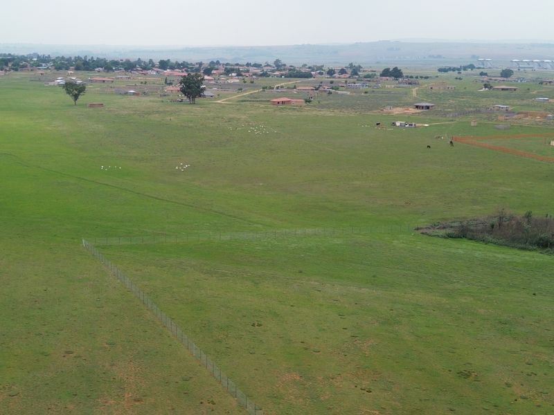 An aerial view of a large, open commercial vacant land plot featuring natural grassland and perimeter wire fencing.
