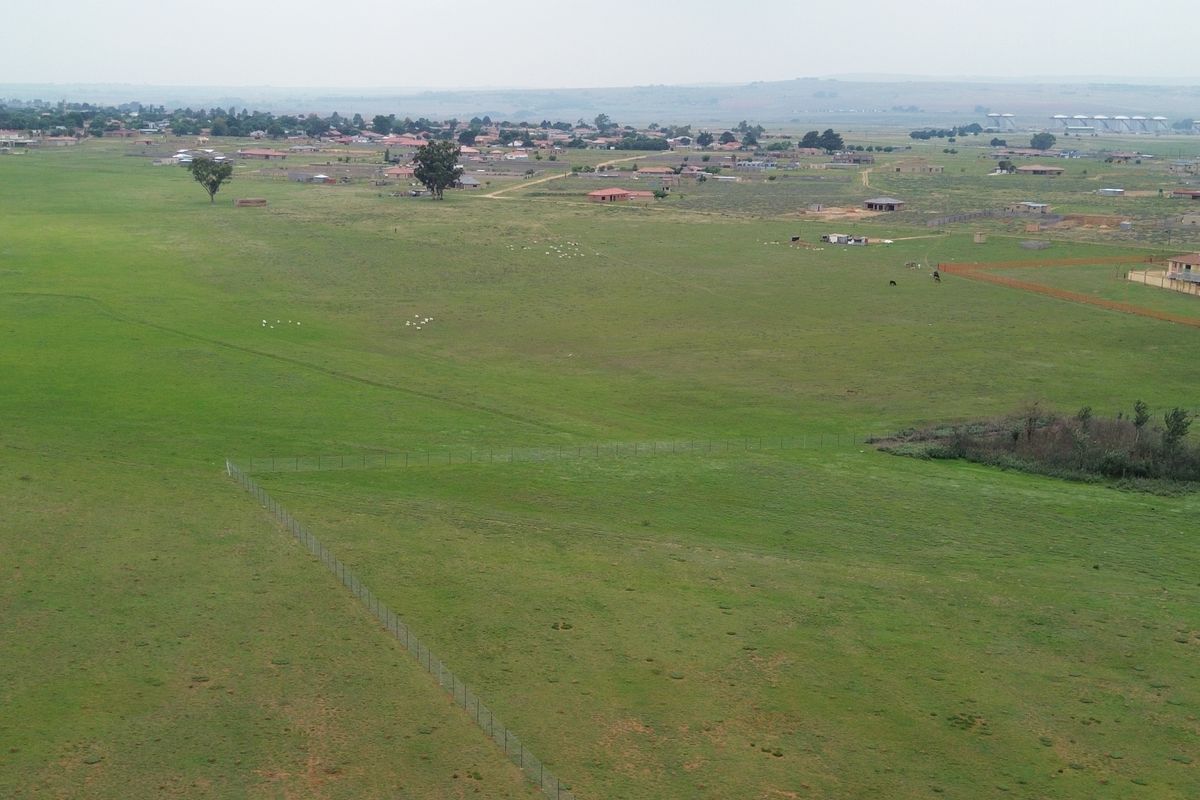 An aerial view of a large, open commercial vacant land plot featuring natural grassland and perimeter wire fencing.