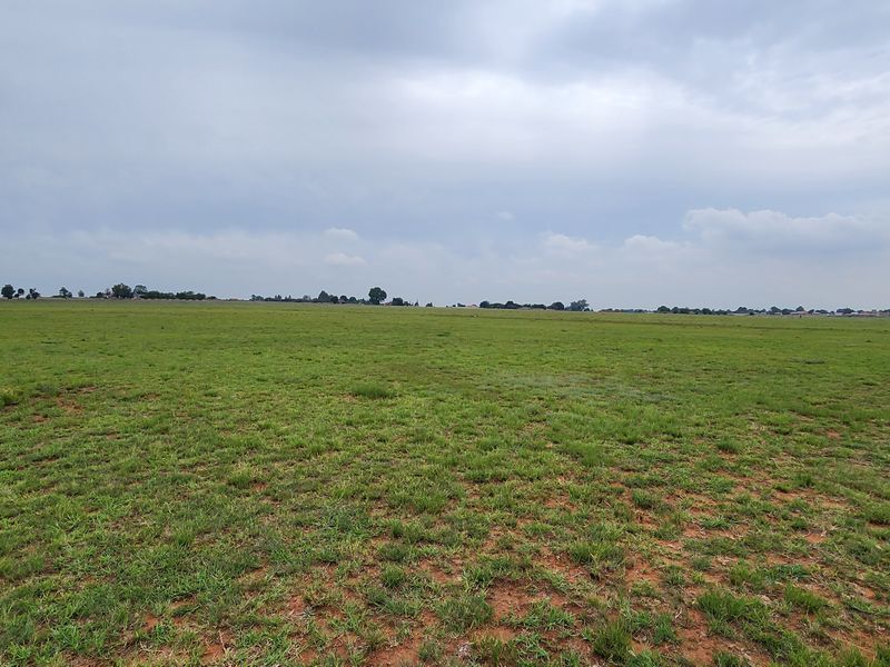 A wide-angle view of the expansive vacant commercial land, featuring open grassland under a cloudy sky.