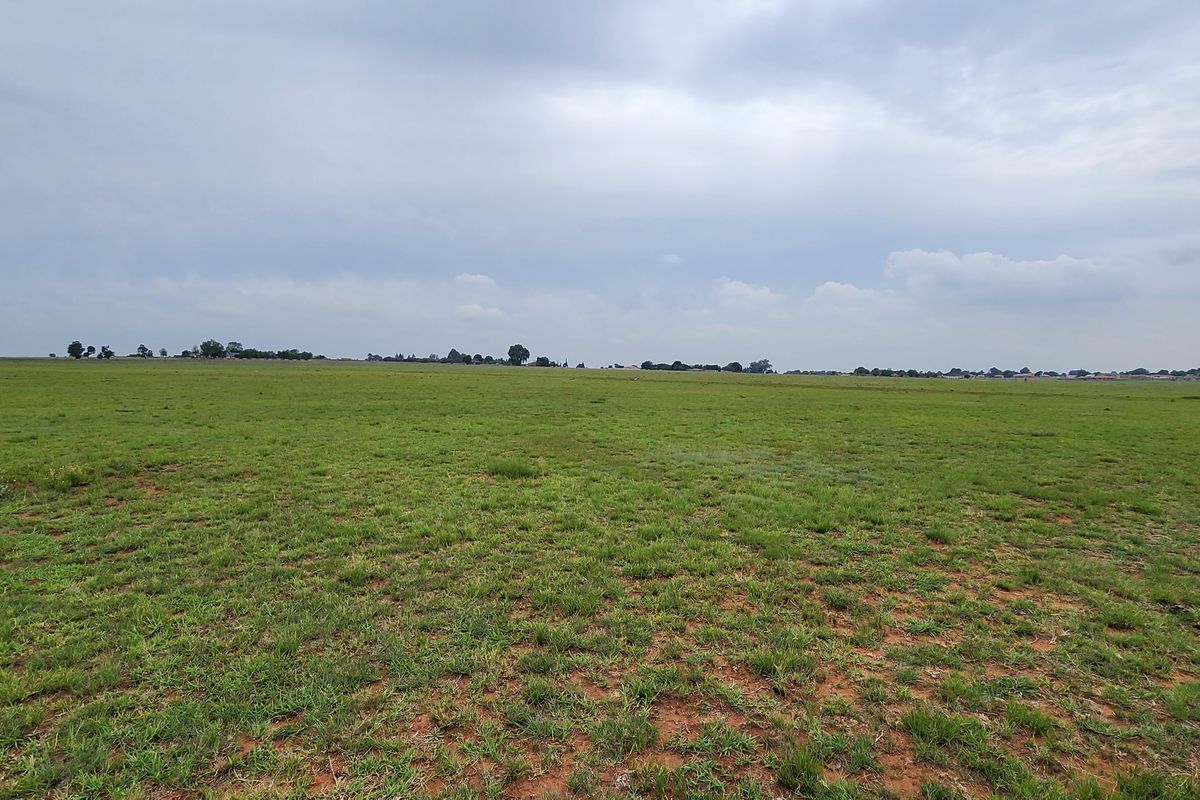 A wide-angle view of the expansive vacant commercial land, featuring open grassland under a cloudy sky.