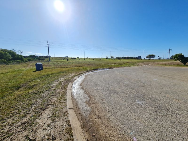 A view of the vacant commercial land featuring paved road access, concrete curbing, and surrounding open landscape.