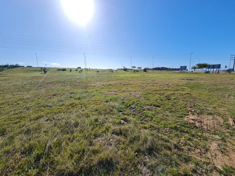 A wide-angle view of a vacant commercial land plot featuring open grass terrain, overhead power lines, and street lighting infrastructure.