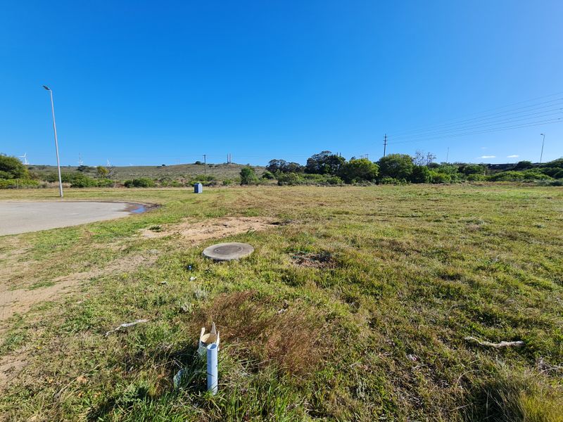 A view of a vacant commercial land plot featuring a paved edge, utility access points, and surrounding natural landscape.