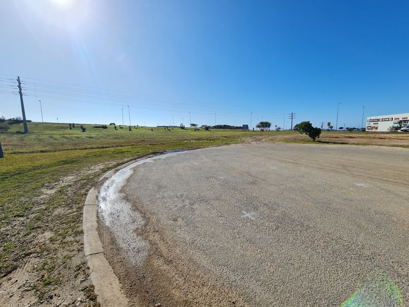A view of a paved road section and adjacent vacant commercial land under a clear blue sky.
