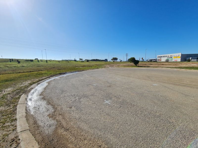 A view of the vacant commercial land featuring a paved access road, concrete curbing, and surrounding undeveloped terrain.