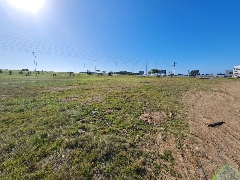 A wide-angle view of a vacant commercial land plot featuring open grassland, utility infrastructure, and access to a nearby road.