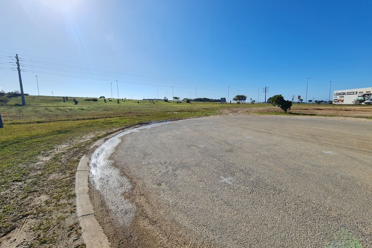 A view of a paved road section and adjacent vacant commercial land under a clear blue sky.