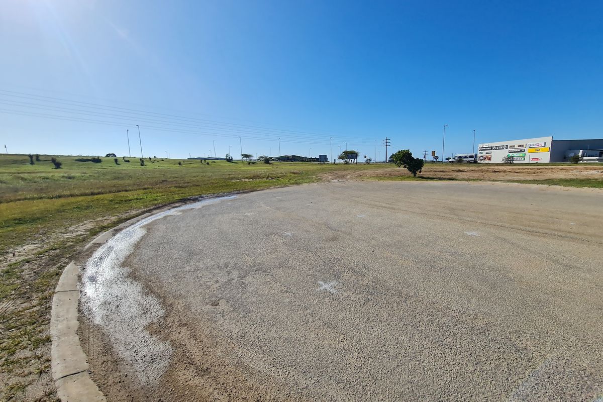 A view of the vacant commercial land featuring a paved access road, concrete curbing, and surrounding undeveloped terrain.