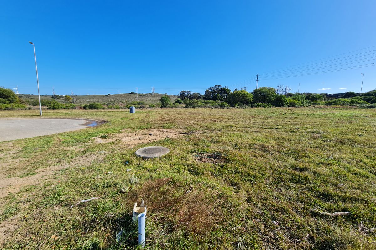 A view of a vacant commercial land plot featuring a paved edge, utility access points, and surrounding natural landscape.