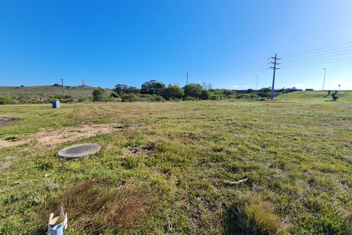 A wide-angle view of a vacant commercial land plot featuring natural grass terrain, utility poles, and an accessible manhole cover.