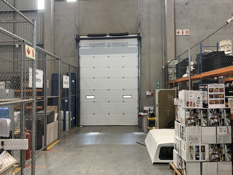 Industrial warehouse utility space featuring a large roller shutter door, concrete flooring, and secure chain-link partitioned storage areas.
