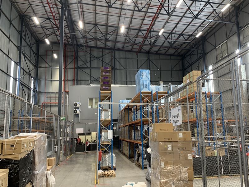 Spacious industrial warehouse facility featuring high-bay ceilings, exposed steel trusses, fire sprinkler systems, and extensive heavy-duty racking for storage and logistics operations.