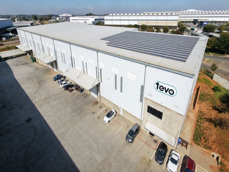 Aerial view of a large industrial warehouse facility featuring a metal-clad exterior, solar panel installation on the roof, and a paved concrete loading yard.
