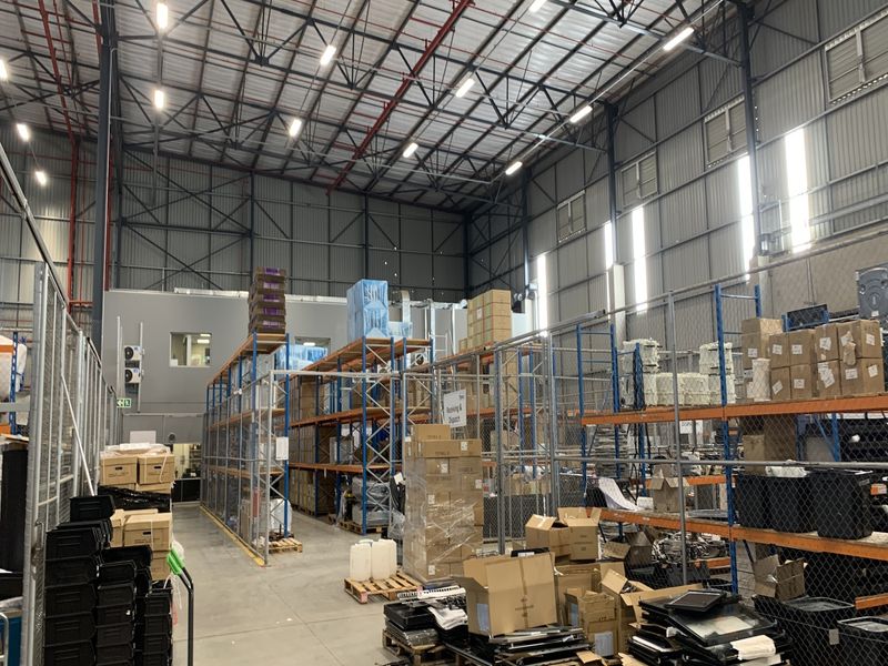 Spacious industrial warehouse featuring high-bay ceilings, exposed steel trusses, concrete flooring, and extensive steel racking systems for storage and logistics operations.