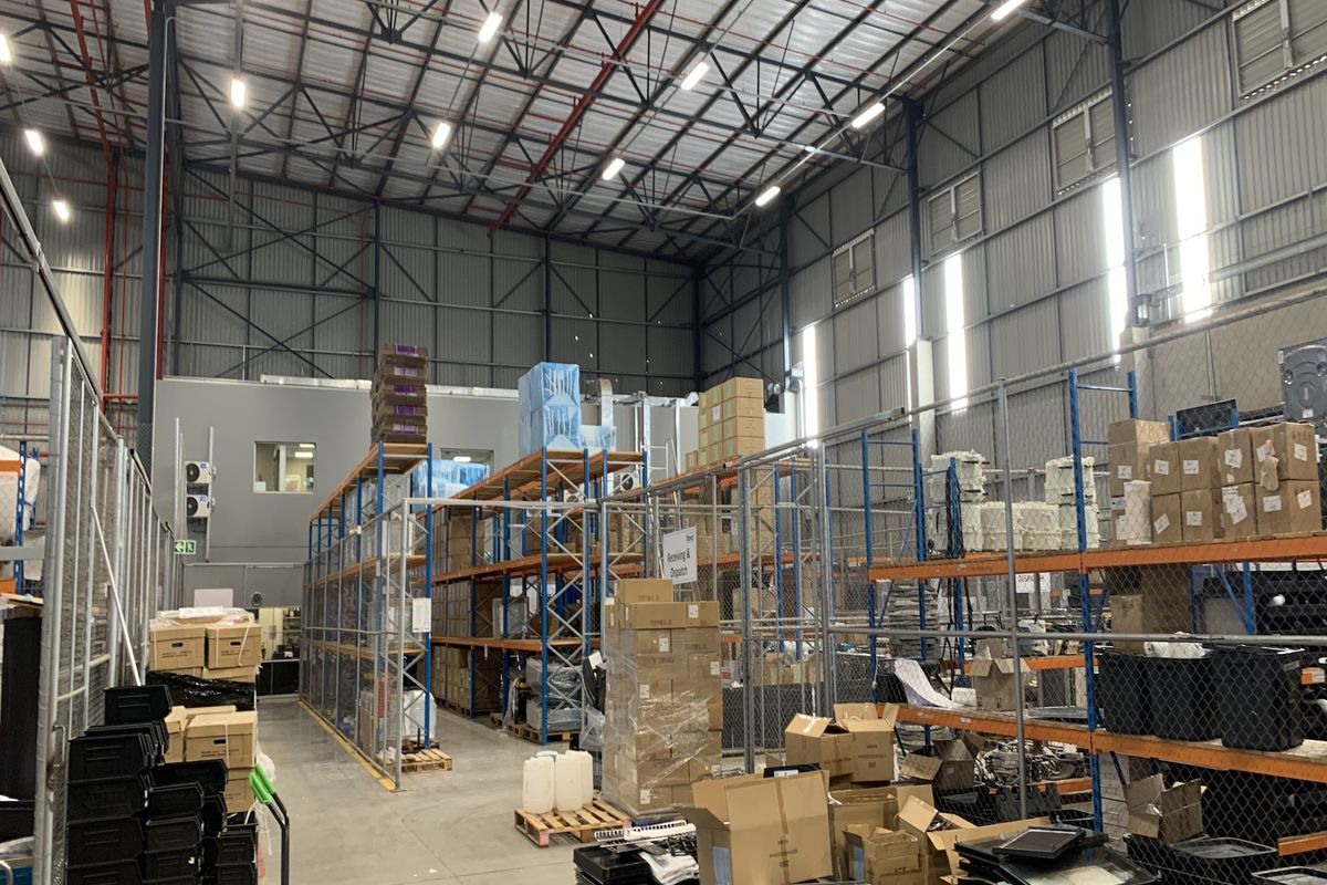 Spacious industrial warehouse featuring high-bay ceilings, exposed steel trusses, concrete flooring, and extensive steel racking systems for storage and logistics operations.