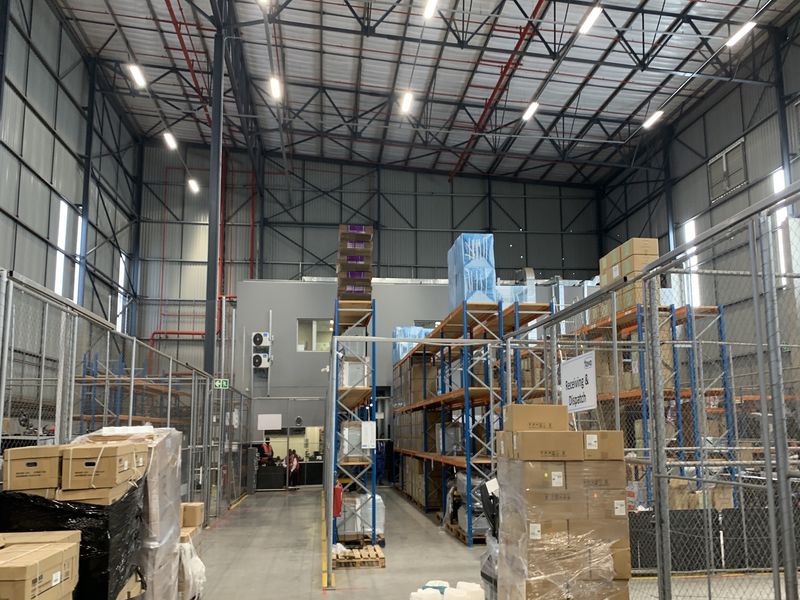 Industrial warehouse space featuring high-clearance ceilings, exposed steel trusses, fire suppression systems, and organized steel racking for receiving and dispatch operations.