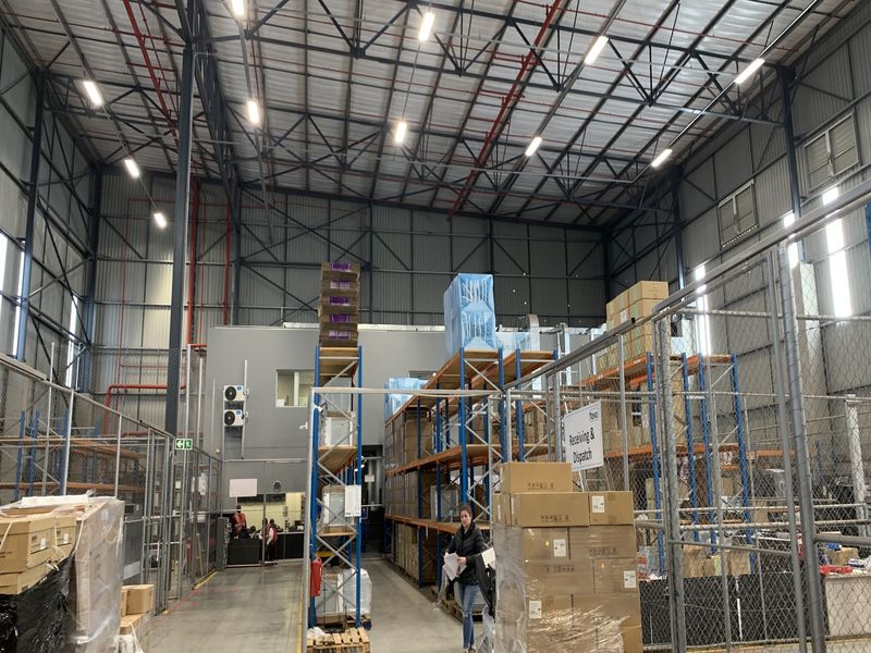 Spacious industrial warehouse facility featuring high ceilings, exposed steel trusses, fire sprinkler systems, and secure partitioned storage areas with concrete flooring.