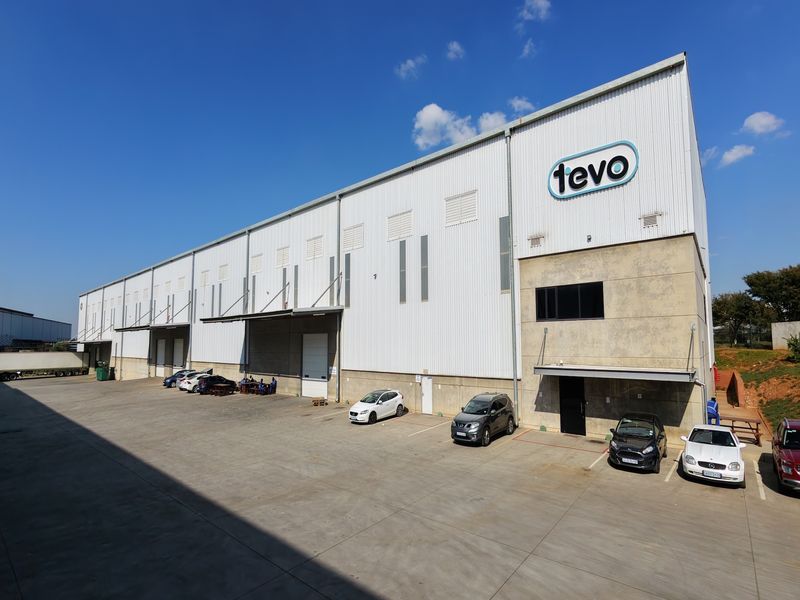 A large industrial warehouse facility featuring corrugated metal cladding, multiple loading bays with roller shutter doors, and a spacious concrete yard area.