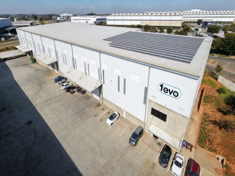 Aerial view of a large industrial warehouse facility featuring extensive solar panel installation on the roof and a paved concrete loading yard.
