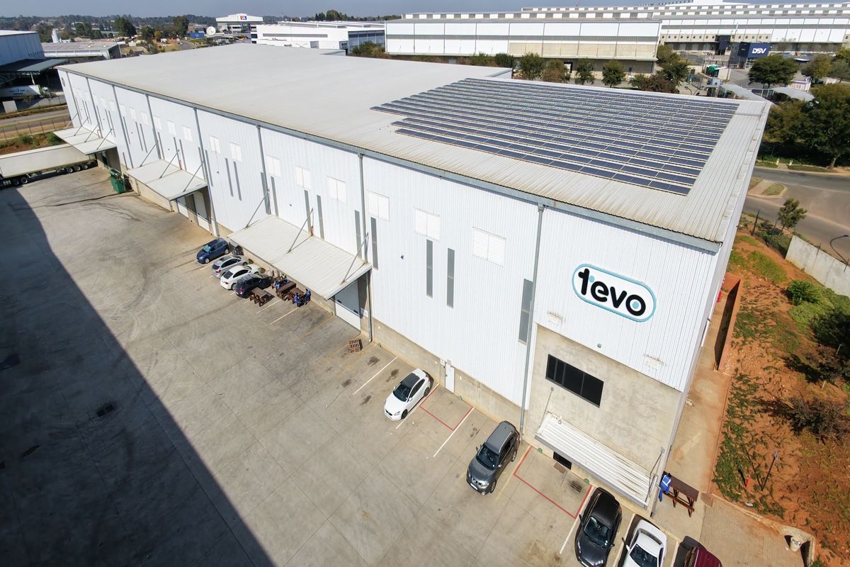 Aerial view of a large industrial warehouse facility featuring extensive solar panel installation on the roof and a paved concrete loading yard.