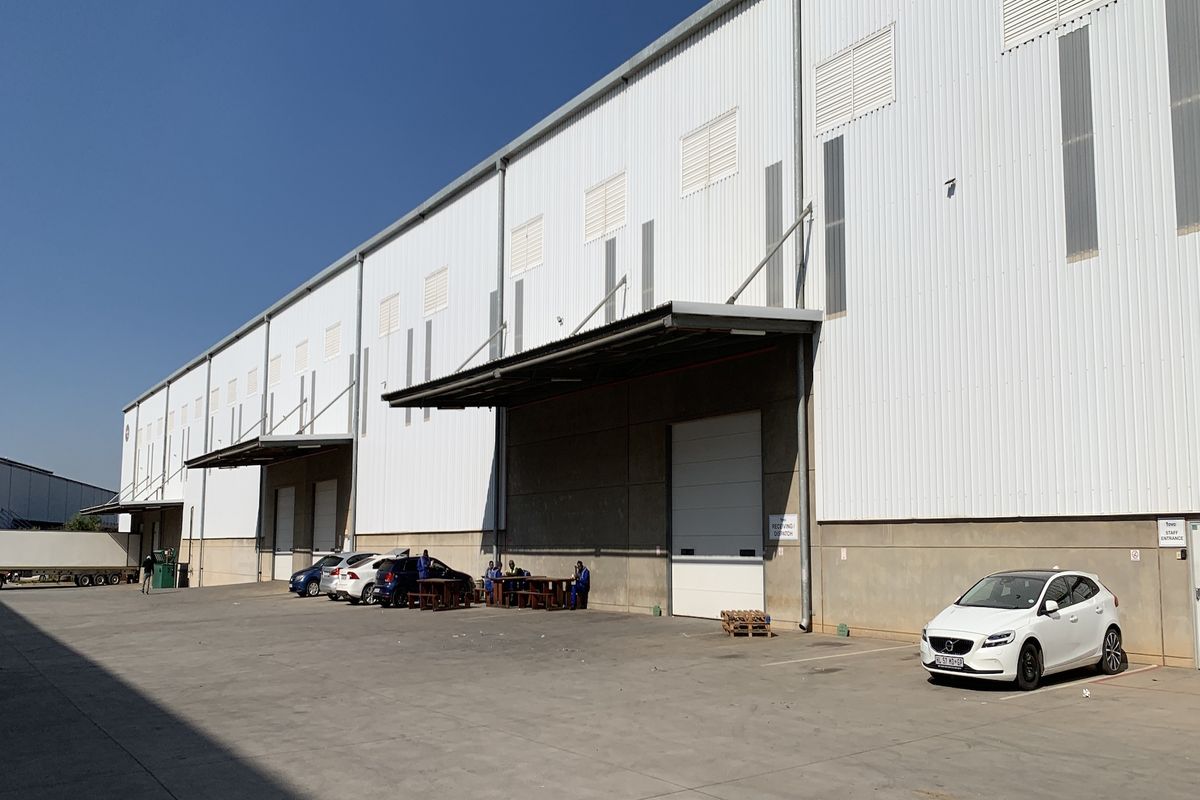 Industrial warehouse exterior featuring corrugated metal cladding, multiple roller shutter loading doors, and a spacious concrete yard area.
