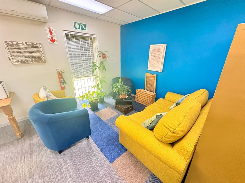 A functional office space featuring carpet tiles, a suspended ceiling with integrated lighting, and a wall-mounted air conditioning unit.
