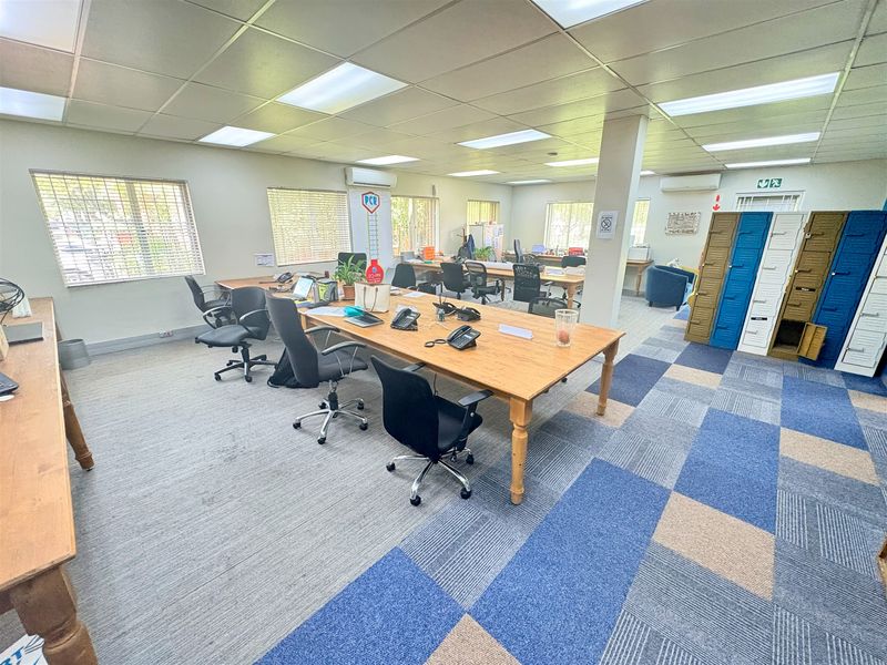 Spacious open-plan office area featuring carpet tiles, suspended ceilings with recessed lighting, integrated air conditioning units, and built-in metal storage lockers.