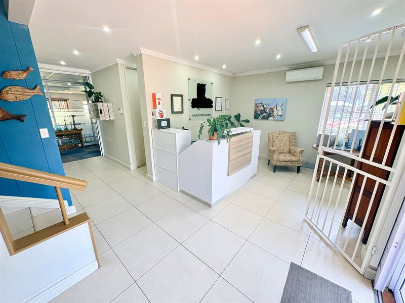 A bright office reception area featuring ceramic floor tiles, a built-in reception desk, recessed lighting, and a wall-mounted air conditioning unit.