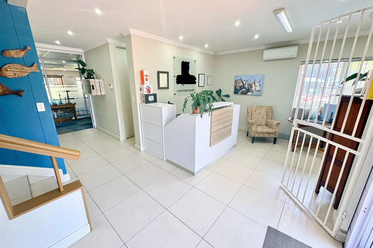 A bright office reception area featuring ceramic floor tiles, a built-in reception desk, recessed lighting, and a wall-mounted air conditioning unit.