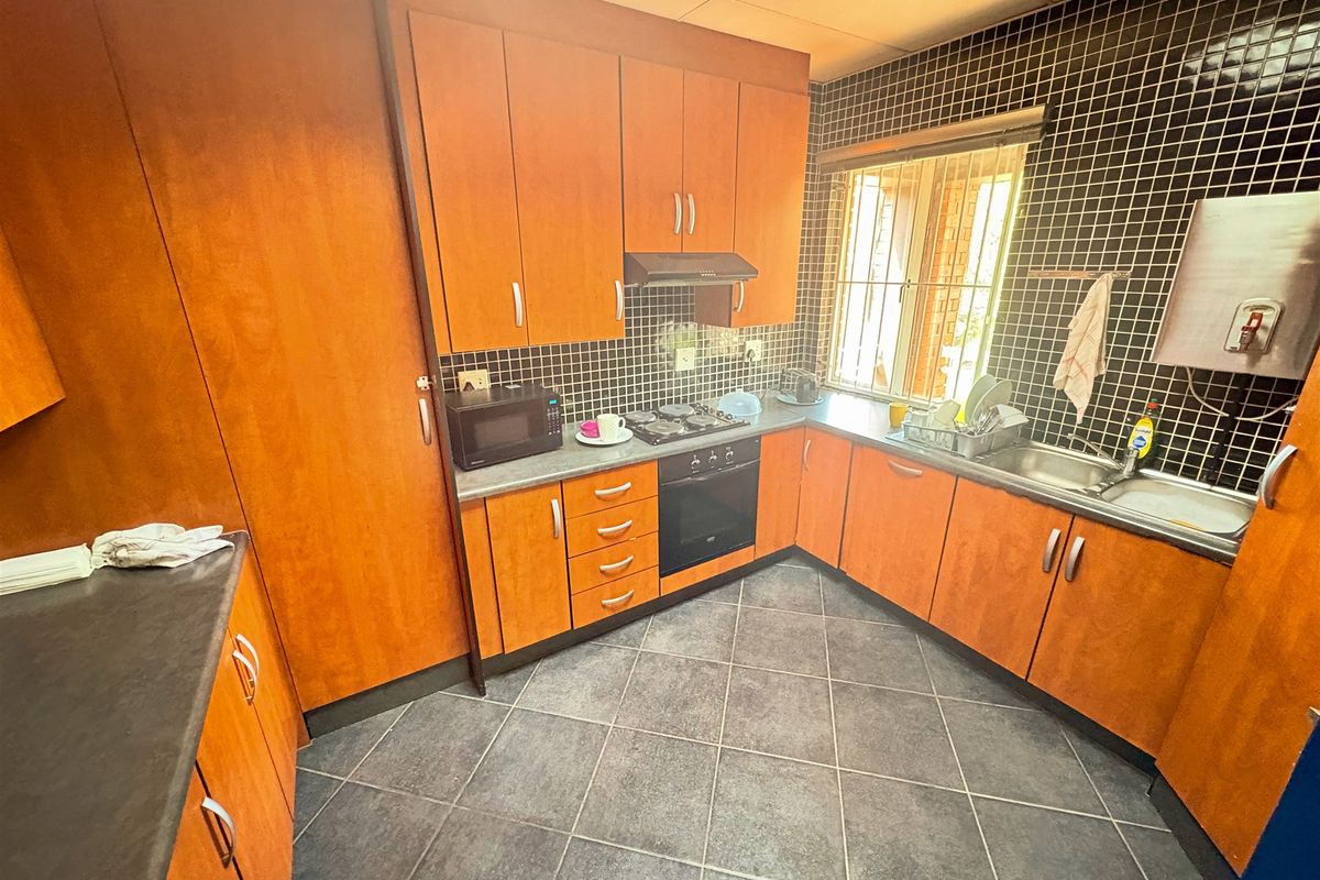 A functional kitchen featuring wood-finish cabinetry, built-in oven and hob, tiled backsplash, and dark floor tiles, offering a practical workspace.