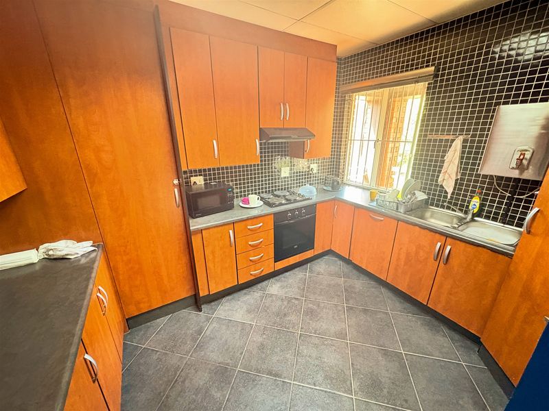 A functional kitchen featuring wood-finish cabinetry, built-in oven and hob, tiled backsplash, and dark floor tiles, offering a practical workspace.