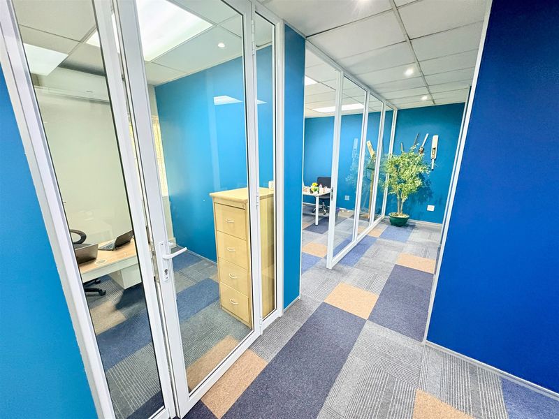 Modern office space featuring glass partition walls, suspended ceilings, and patterned carpet tiles, creating a bright and professional work environment.
