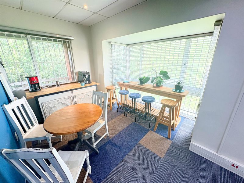 A functional office space featuring carpet tiles, large windows with security bars, venetian blinds, and integrated electrical power points.