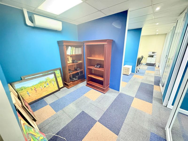 A functional office space featuring blue accent walls, carpet tile flooring, a suspended ceiling, and a glass partition wall for a modern professional layout.