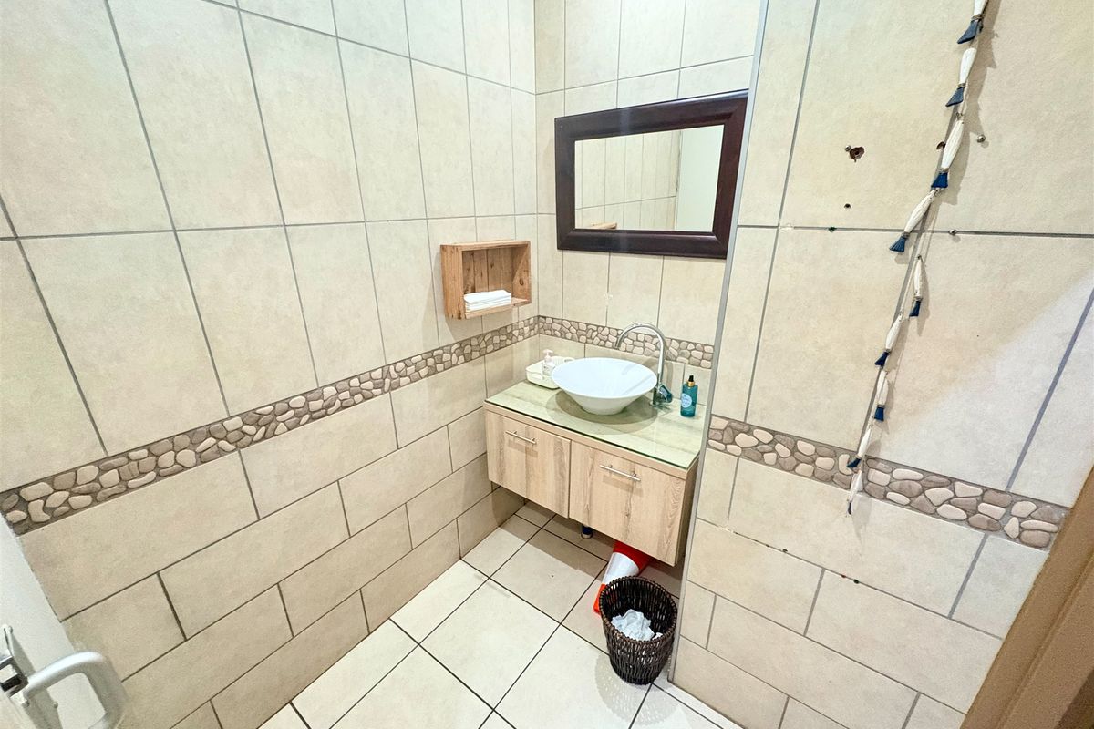 A compact bathroom featuring tiled walls with a decorative stone border, a wall-mounted vanity with a vessel sink, and a framed mirror.