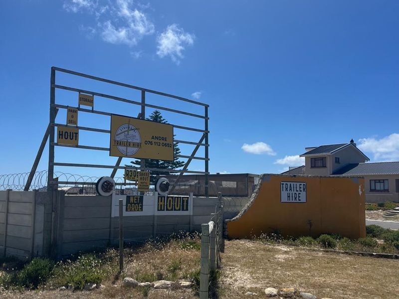 Exterior view of a commercial property featuring a large metal signage frame, precast concrete boundary walls, and razor wire security fencing.