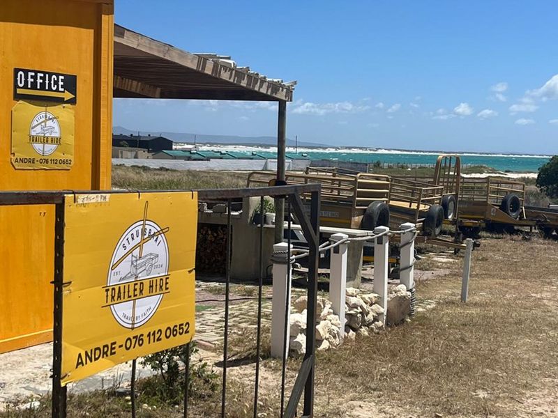 Exterior view of a business premises featuring a metal gate, timber pergola, and signage, with coastal views in the background.