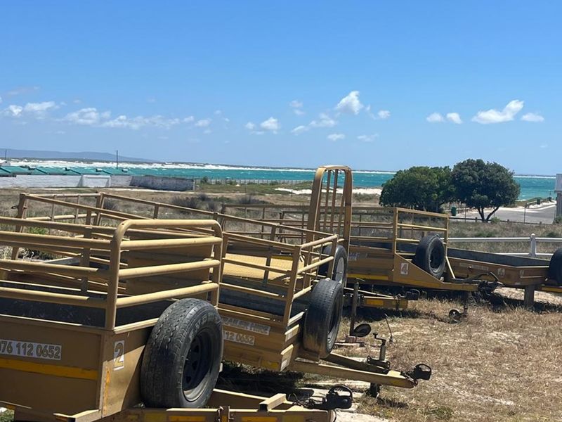An outdoor area featuring a line of trailers parked on a dirt lot with a coastal view in the background.