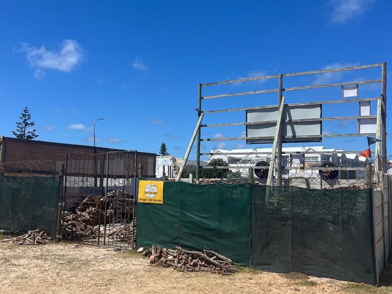 Exterior view of a commercial property site featuring a large billboard frame, metal security fencing with razor wire, and a concrete boundary wall.