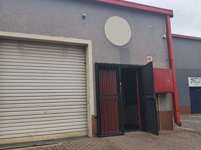 Exterior view of a commercial retail unit featuring a roller shutter door, security gate entrance, and paved frontage.
