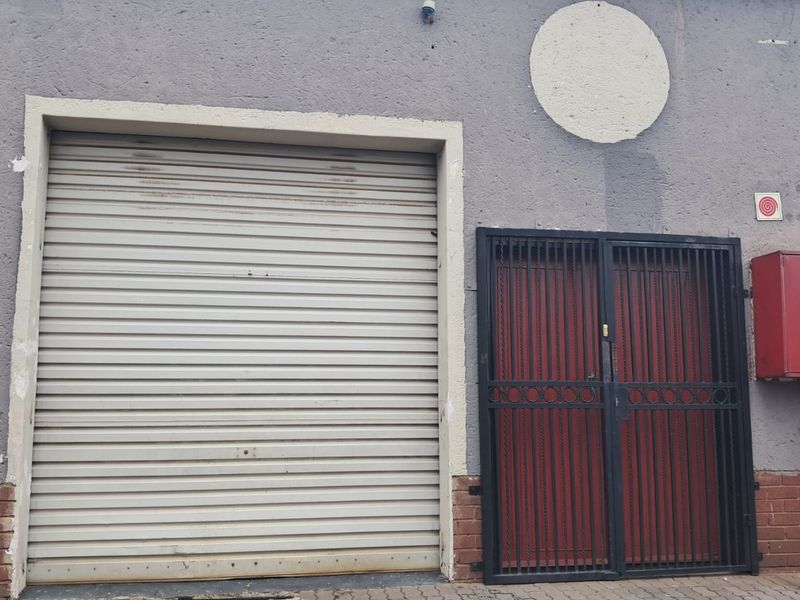 Exterior view of a retail property featuring a metal roller shutter door, a security gate, and a wall-mounted fire hose cabinet.