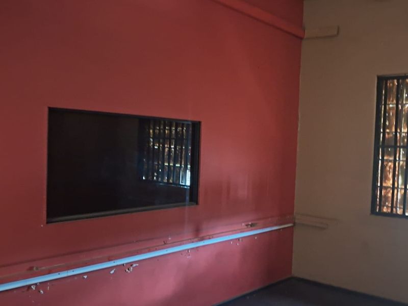 An interior retail space featuring red painted walls, a built-in viewing window, and windows secured with metal bars.