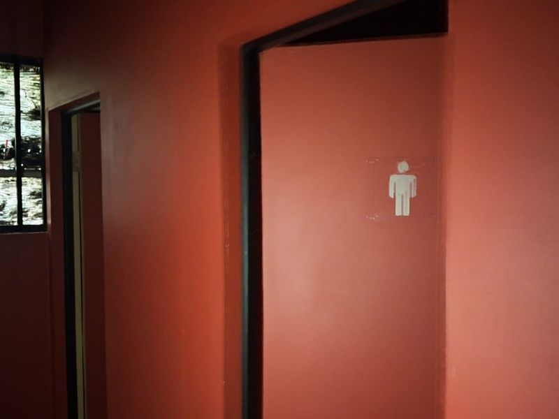 A dimly lit hallway in a retail property featuring a restroom door with signage and a small window with security bars.