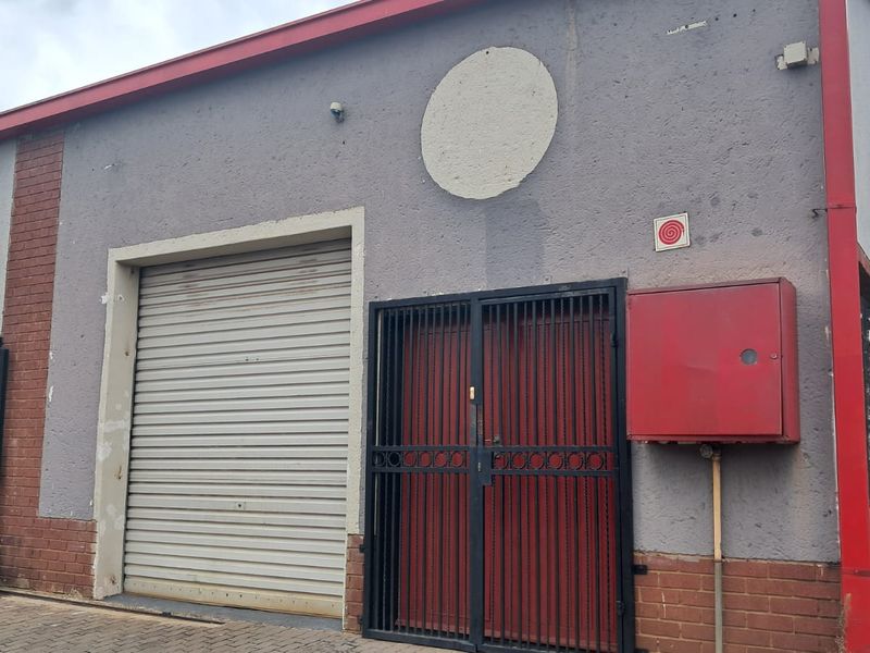 Exterior view of a retail property featuring a roller shutter door, security gate, and red fire equipment cabinet on a textured facade.